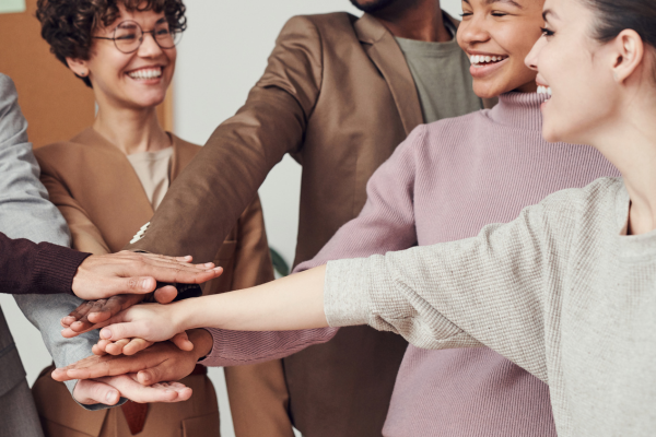A diverse group of people smiling and stacking their hands together in teamwork and unity.
